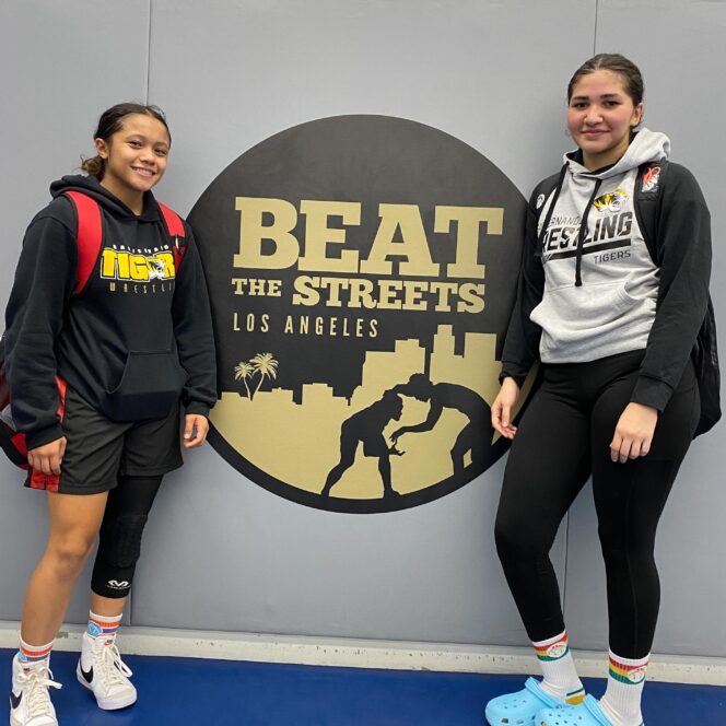 Two female wrestlers pose with program's logo